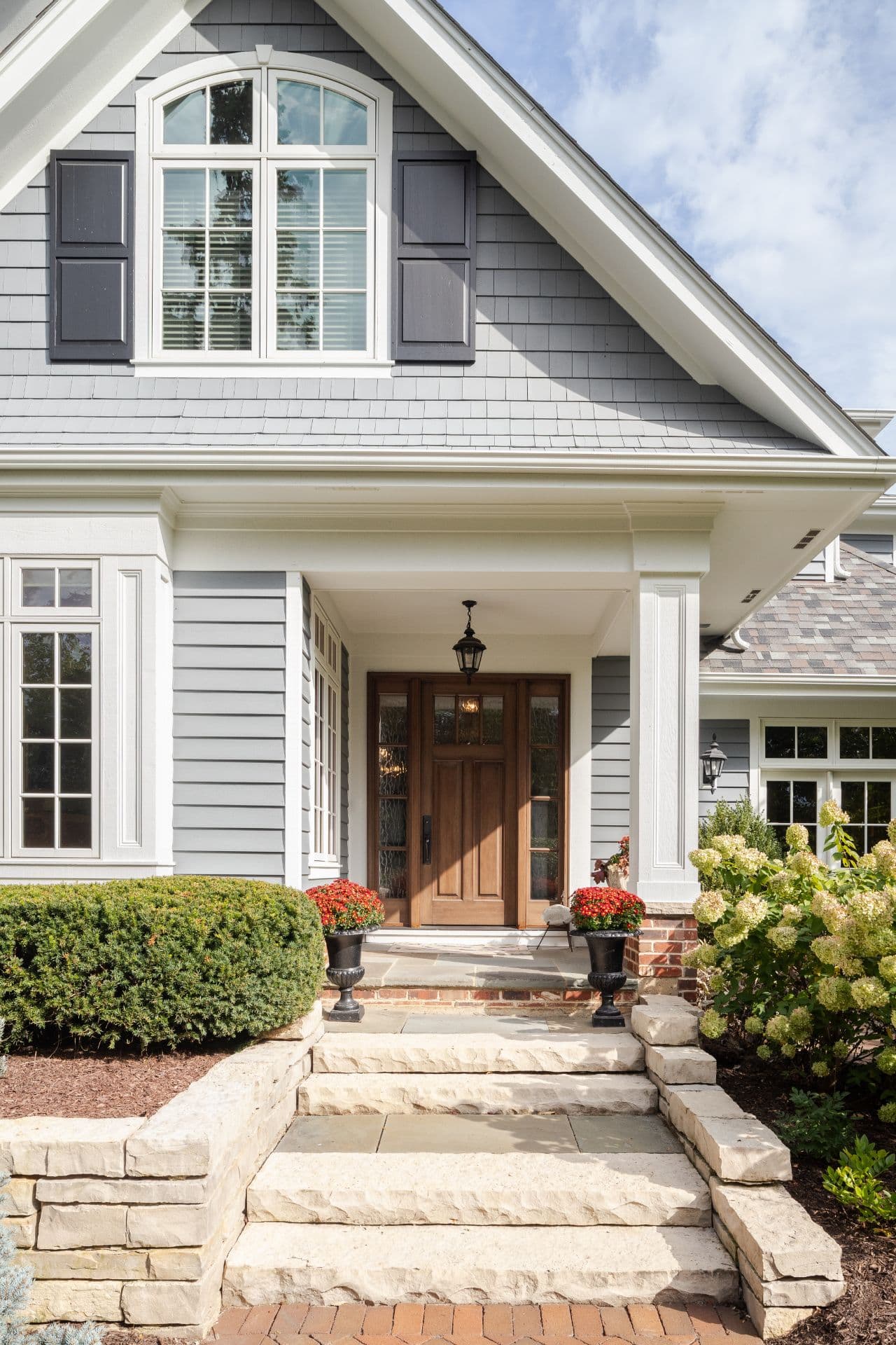 Covered front entry of a home with stone steps and planters of autumn mums