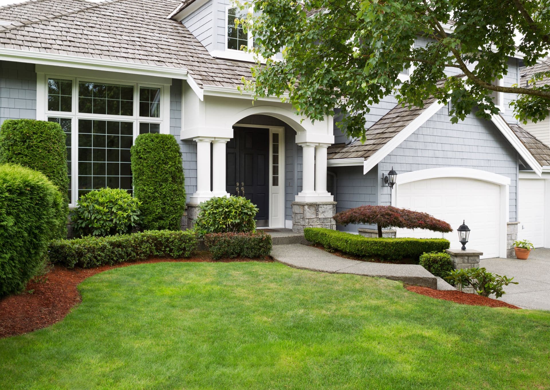 Front exterior of a shingled home with a manicured lawn, clipped hedges and a double garage